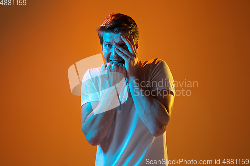 Image of Caucasian beautiful young man\'s portrait on gradient orange studio background, emotional and expressive. Copyspace for ad.