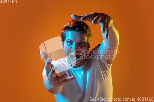 Image of Caucasian beautiful young man\'s portrait on gradient orange studio background, emotional and expressive. Copyspace for ad.