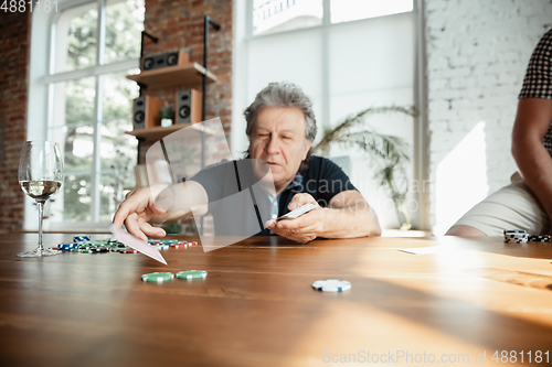 Image of Senior man playing cards and drinking wine with friends, looks happy