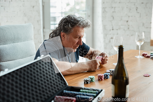 Image of Senior man playing cards and drinking wine with friends, looks happy