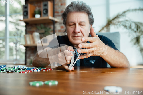 Image of Senior man playing cards and drinking wine with friends, looks happy