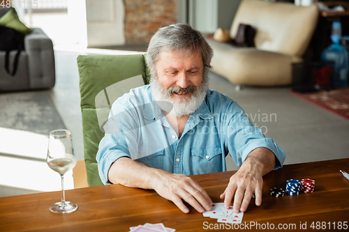 Image of Senior man playing cards and drinking wine with friends, looks happy