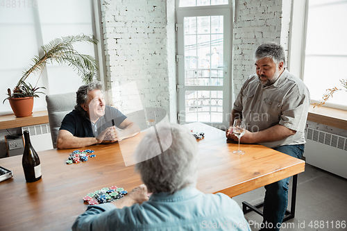 Image of Group of happy mature friends playing cards and drinking wine