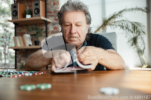 Image of Senior man playing cards and drinking wine with friends, looks happy