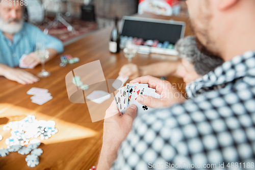 Image of Close up group of happy mature friends playing cards and drinking wine