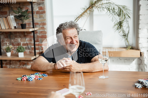 Image of Senior man playing cards and drinking wine with friends, looks happy