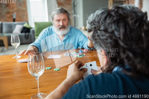 Image of Two happy mature friends playing cards and drinking wine