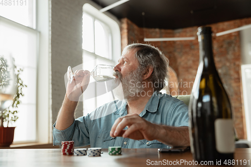 Image of Senior man playing cards and drinking wine with friends, looks happy
