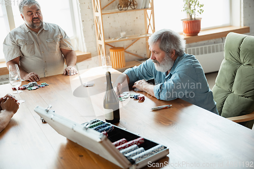Image of Two happy mature friends playing cards and drinking wine