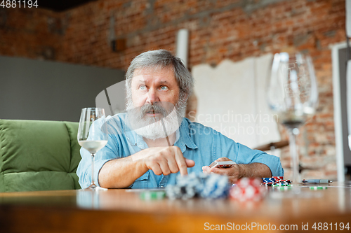 Image of Senior man playing cards and drinking wine with friends, looks happy