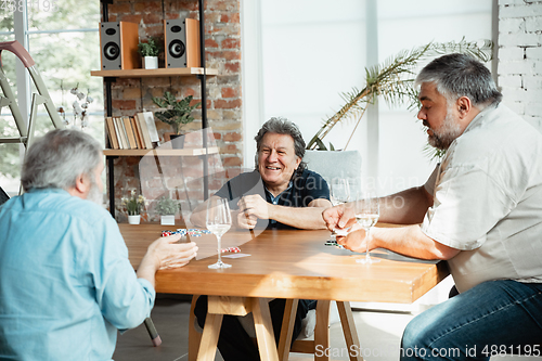 Image of Group of happy mature friends playing cards and drinking wine