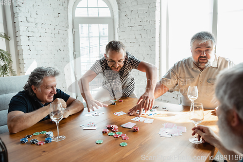 Image of Group of happy mature friends playing cards and drinking wine