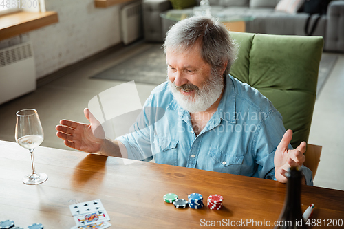 Image of Senior man playing cards and drinking wine with friends, looks happy