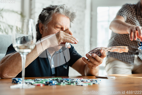 Image of Two happy mature friends playing cards and drinking wine