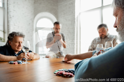Image of Group of happy mature friends playing cards and drinking wine