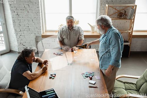 Image of Group of happy mature friends playing cards and drinking wine