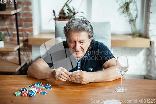 Image of Senior man playing cards and drinking wine with friends, looks happy