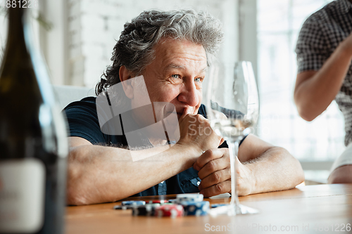 Image of Senior man playing cards and drinking wine with friends, looks happy