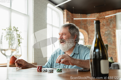 Image of Senior man playing cards and drinking wine with friends, looks happy