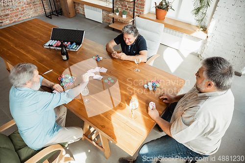 Image of Group of happy mature friends playing cards and drinking wine