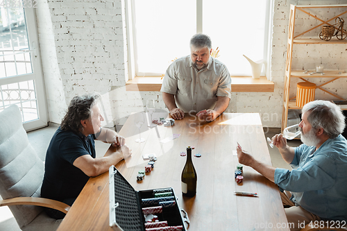 Image of Group of happy mature friends playing cards and drinking wine