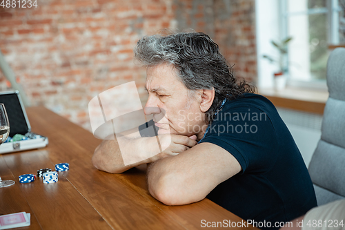 Image of Senior man playing cards and drinking wine with friends, looks happy