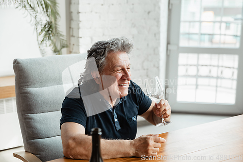 Image of Senior man playing cards and drinking wine with friends, looks happy