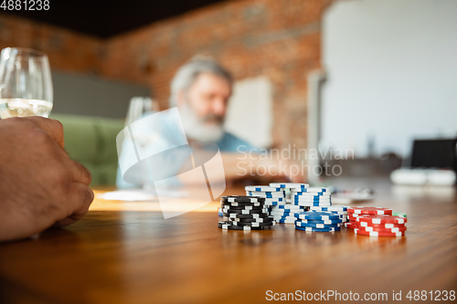 Image of Close up group of happy mature friends playing cards and drinking wine