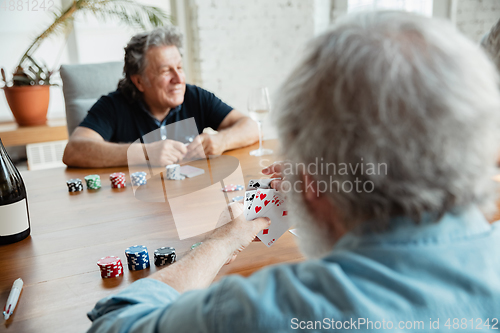 Image of Two happy mature friends playing cards and drinking wine