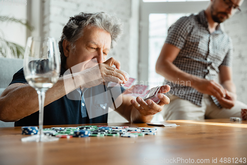 Image of Two happy mature friends playing cards and drinking wine