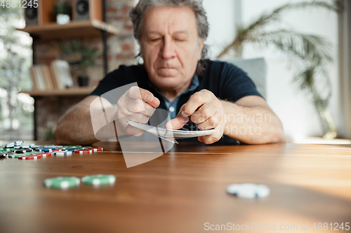 Image of Senior man playing cards and drinking wine with friends, looks happy