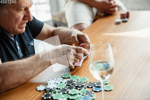 Image of Senior man playing cards and drinking wine with friends, looks happy