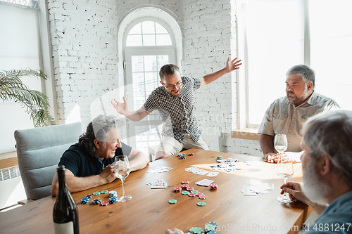 Image of Group of happy mature friends playing cards and drinking wine