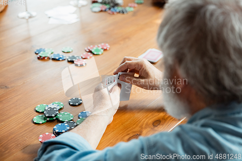 Image of Senior man playing cards and drinking wine with friends, looks happy