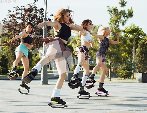 Image of Beautiful women in sportswear jumping in a kangoo jumps shoes at the street on summer\'s sunny day