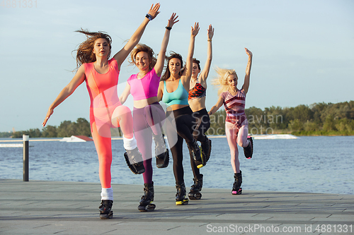 Image of Beautiful women in sportswear jumping in a kangoo jumps shoes at the street on summer\'s sunny day