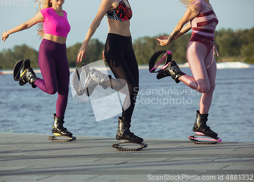 Image of Beautiful women in sportswear jumping in a kangoo jumps shoes at the street on summer\'s sunny day