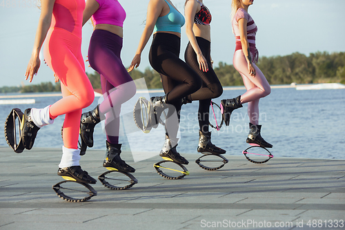 Image of Beautiful women in sportswear jumping in a kangoo jumps shoes at the street on summer\'s sunny day