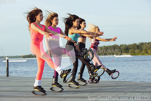 Image of Beautiful women in sportswear jumping in a kangoo jumps shoes at the street on summer\'s sunny day