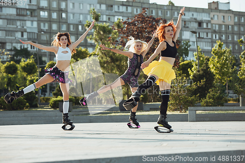 Image of Beautiful women in sportswear jumping in a kangoo jumps shoes at the street on summer\'s sunny day