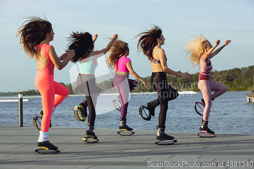 Image of Beautiful women in sportswear jumping in a kangoo jumps shoes at the street on summer\'s sunny day