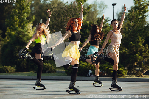 Image of Beautiful women in sportswear jumping in a kangoo jumps shoes at the street on summer\'s sunny day