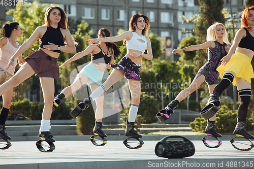 Image of Beautiful women in sportswear jumping in a kangoo jumps shoes at the street on summer\'s sunny day