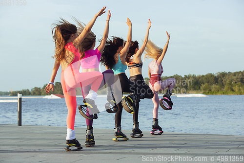 Image of Beautiful women in sportswear jumping in a kangoo jumps shoes at the street on summer\'s sunny day