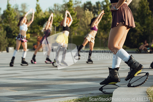 Image of Beautiful women in sportswear jumping in a kangoo jumps shoes at the street on summer\'s sunny day