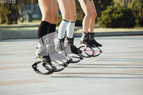 Image of Beautiful women in sportswear jumping in a kangoo jumps shoes at the street on summer\'s sunny day