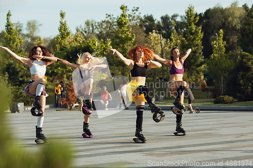 Image of Beautiful women in sportswear jumping in a kangoo jumps shoes at the street on summer\'s sunny day