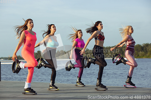Image of Beautiful women in sportswear jumping in a kangoo jumps shoes at the street on summer\'s sunny day
