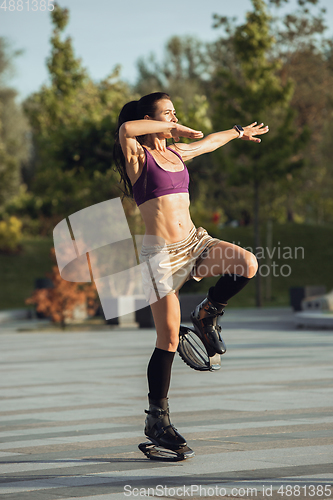 Image of Beautiful woman in sportswear jumping in a kangoo jumps shoes at the street on summer\'s sunny day