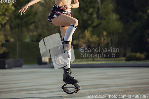 Image of Beautiful woman in sportswear jumping in a kangoo jumps shoes at the street on summer\'s sunny day